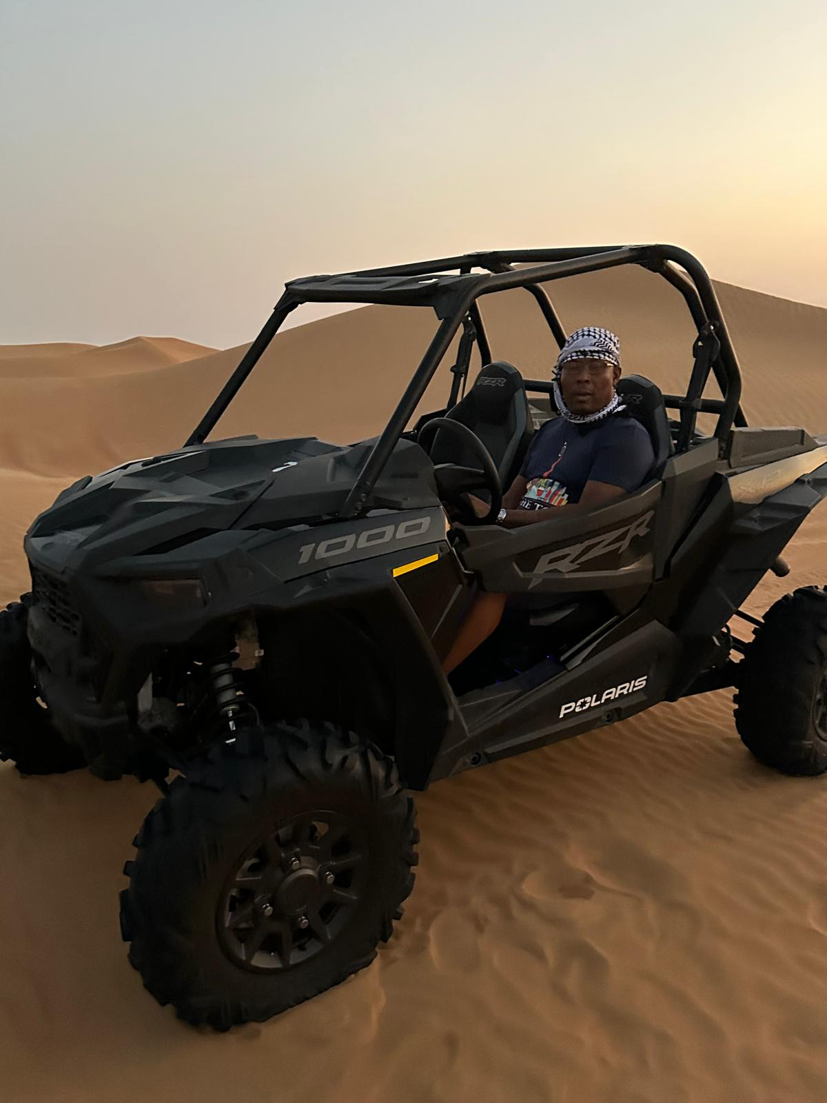 A traveler driving a dune buggy across desert sand dunes at sunset