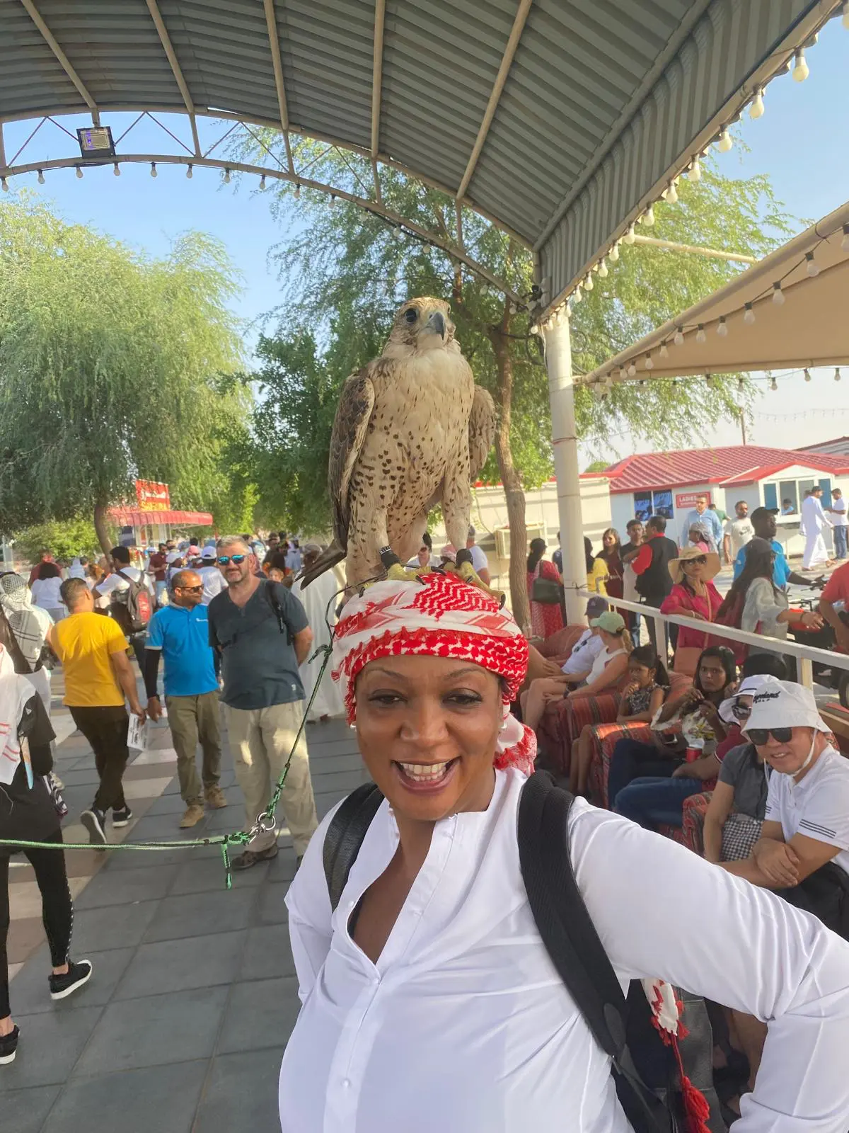 A smiling traveler with a falcon perched on her headscarf at a desert camp