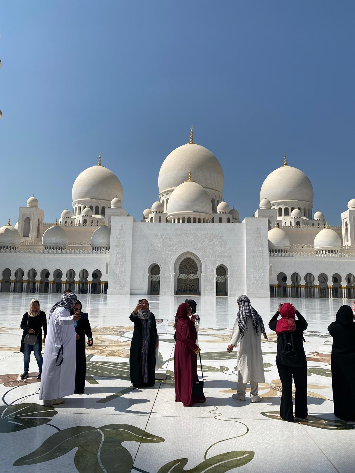 Travelers visiting the white domes and courtyard of the Sheikh Zayed Grand Mosque